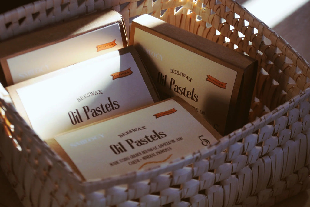 Multiple boxes of all-natural beeswax oil pastels in a woven basket, emphasizing eco-friendly and non-toxic art supplies