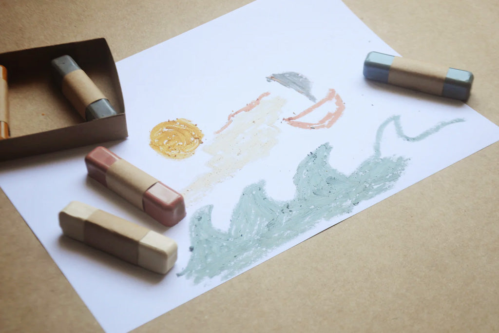 Eco-friendly, non-toxic beeswax oil pastels and child’s drawing of ocean waves, sun, and sailboat on white paper