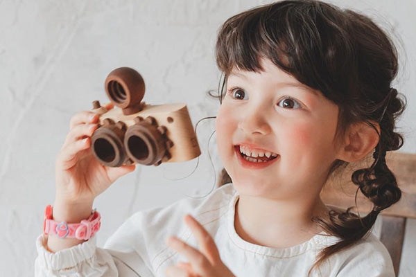 photo shows a child holding a two lens wooden toy camera. this wooden toy is made of walnut and beech wood. she loves playing wooden toys.