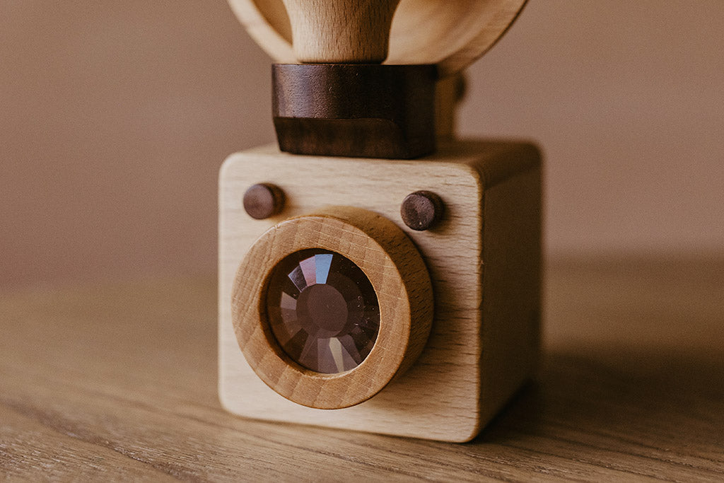 A closed up of the Brownie wooden toy camera that is inspired by the vintage Kodak Brownie camera. It features a detachable bulb-style flash and kaleidoscope lens.