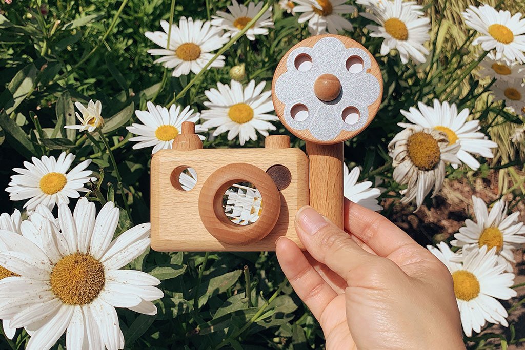 Photo shows a child holding wooden toy camera with the spring white flowers as background. Inspired by the vintage 35MM camera, the toy camera comes with a vintage flash, and it’s the best first camera for encouraging children’s creativity. Wooden toys are safer than plastic toys because they are made of non-toxic and biodegradable materials. When choosing wooden toys, wooden toy camera is the essential type of toy for your child’s open-ended playtime.