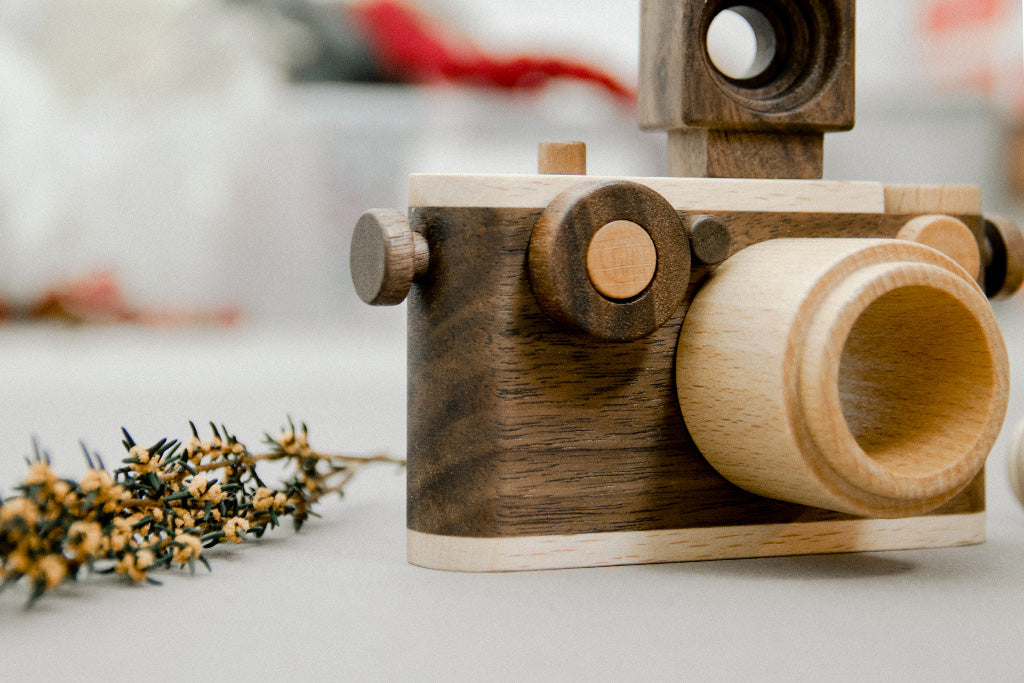 A close-up of a handcrafted wooden toy camera made from walnut and beechwood, featuring a kaleidoscope lens, a detachable vintage-style flash, and clickable buttons, highlighting its intricate details and sustainable materials