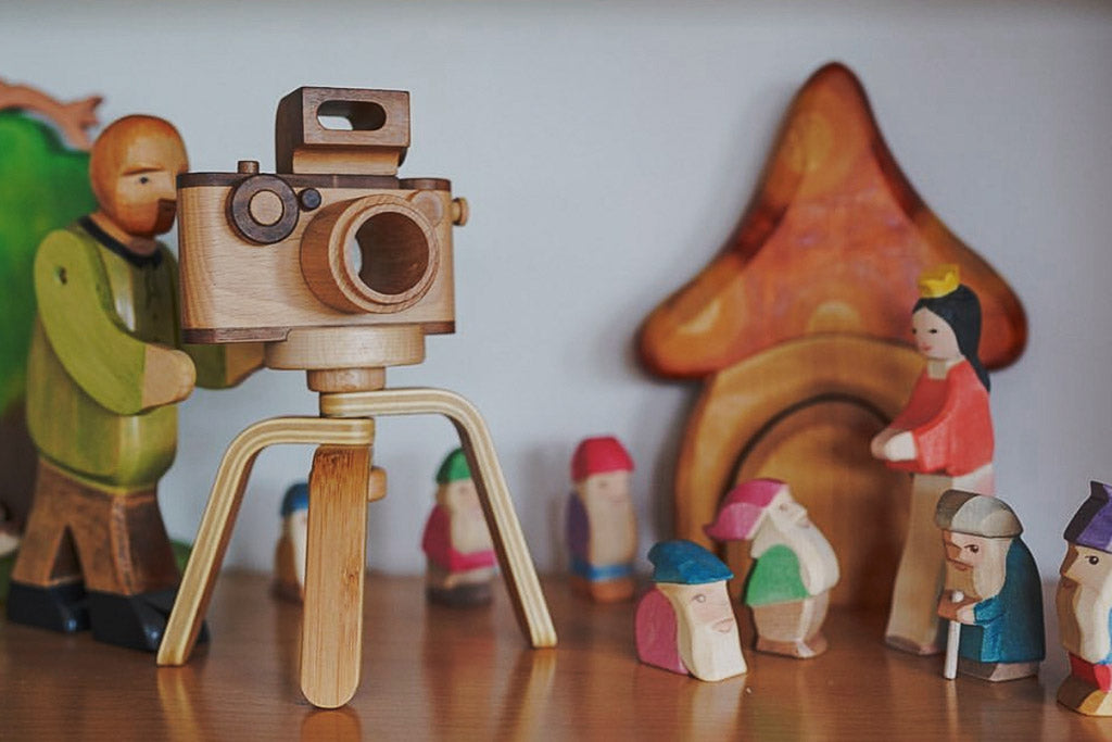 Photo shows a wooden doll pretending to take a photo with a wooden toy camera on tripod. Wooden toys are safer than plastic toys because they are made of non-toxic and biodegradable materials. When choosing wooden toys, wooden toy camera is the essential type of toy for your child’s open-ended playtime. Inspired by the vintage 35MM camera, the toy camera comes with a vintage flash, and it’s the best first camera for encouraging children’s creativity. 