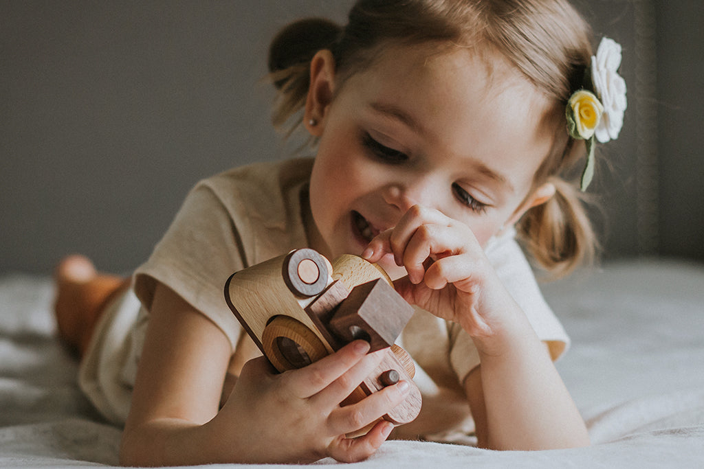 Child smiling while holding a wooden toy camera with a vintage-inspired design, pretend-playing as a photographer. Featuring a vintage flash, this non-toxic and biodegradable wooden toy encourages creativity and open-ended playtime.