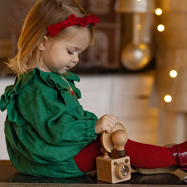 A little girl is holding a wooden toy camera that is inspired by vintage brownie camera. 