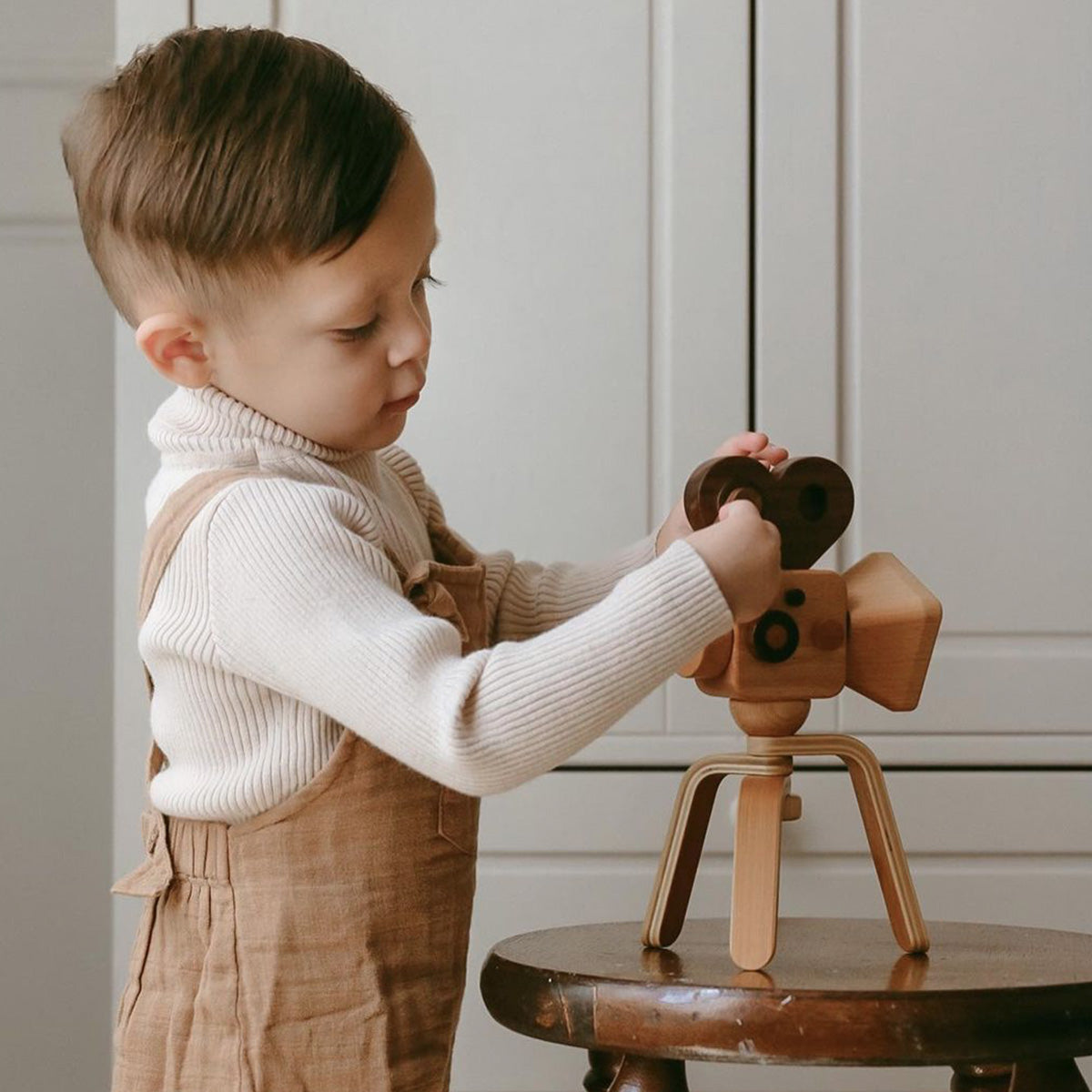 A boy creatively plays with a wooden toy camera featuring a super 16 video camera design, enhancing his imaginative playtime