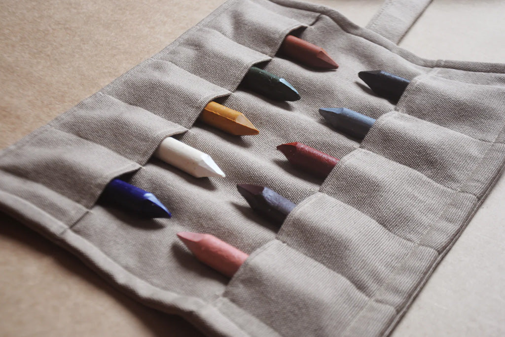 Set of ten organic beeswax crayons in earthy and primary colors stored in a gray canvas roll-up pouch